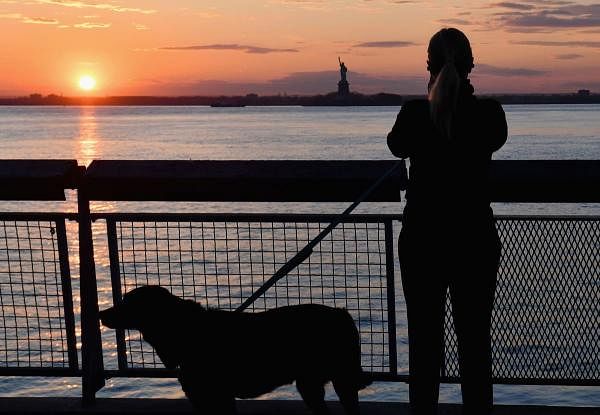 A woman walking her dog stops to look at the sunset over the Statue of Liberty. Credit: AFP Photo