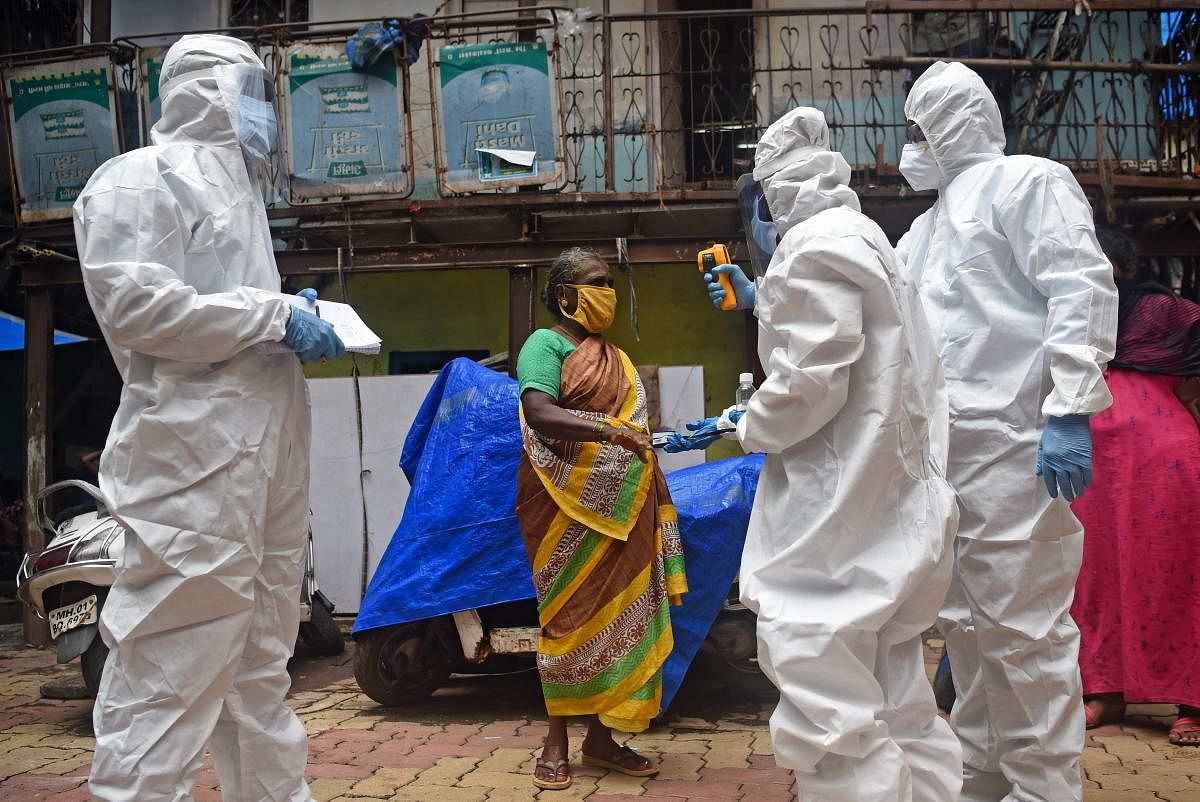 Medical volunteers wearing Personal Protective Equipment (PPE) gear take temperature reading of a woman as they conduct a door-to-door medical screening inside Dharavi slums to fight against the spread of the Covid-19. Credit: PTI