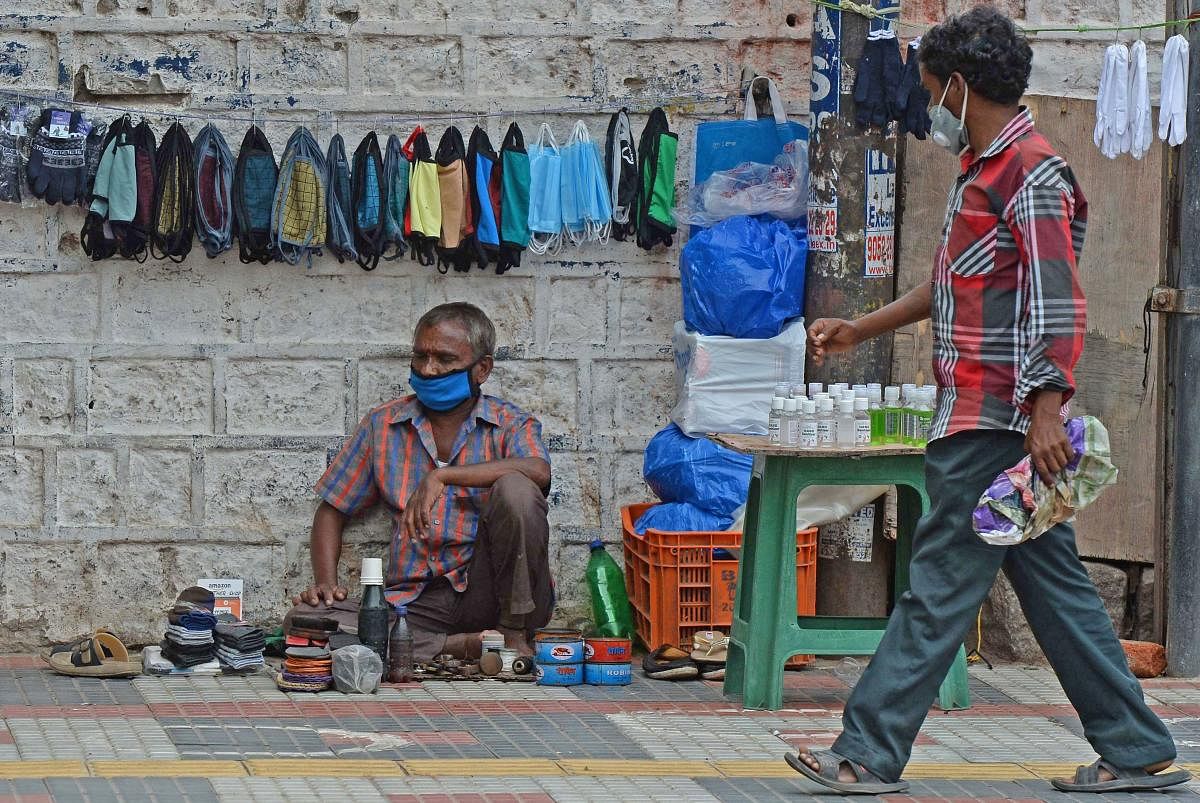 A pedestrian walks past a cobbler selling facemasks and sanitizers on the roadside after the authorities eased restrictions imposed as a preventive measure against the spread of the COVID-19 coronavirus, in Hyderabad on July 10, 2020. Credit: AFP Photo