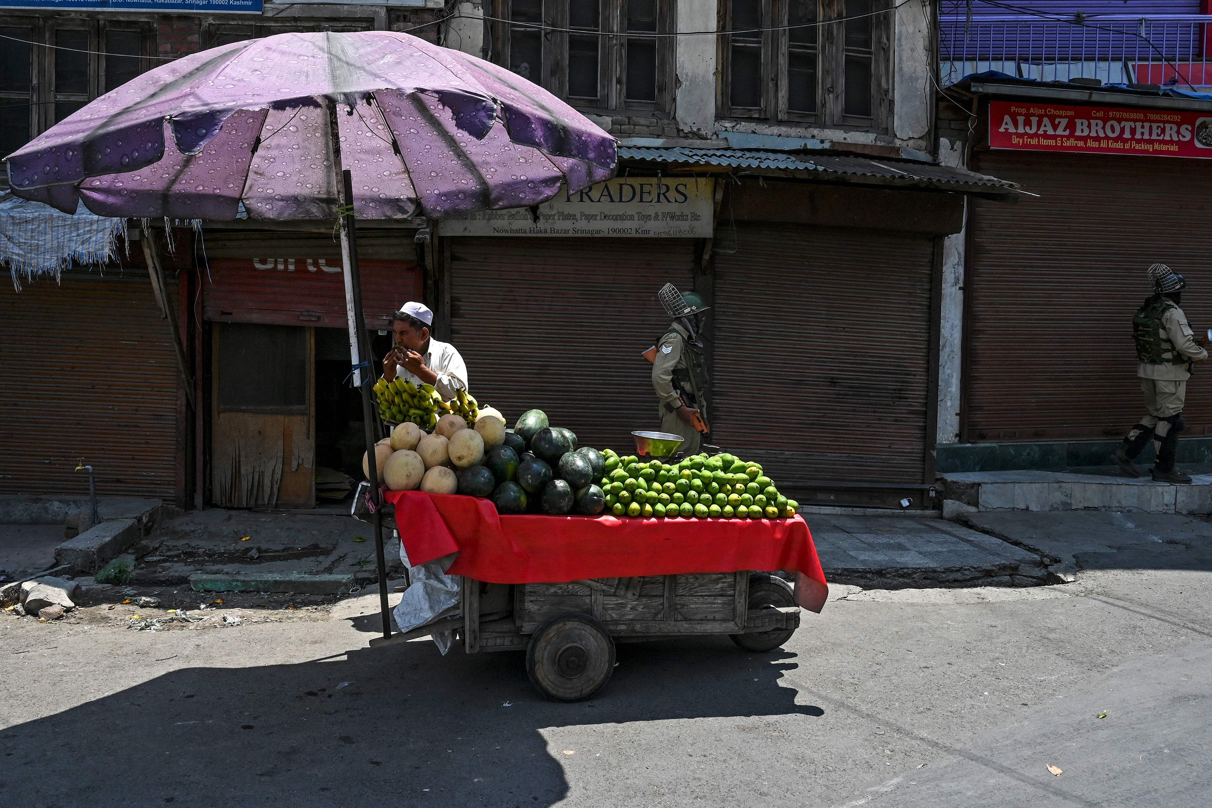 A street vendor sells fruits as security personnel stand guard on a street where most shops are shut. Credits: AFP Photo