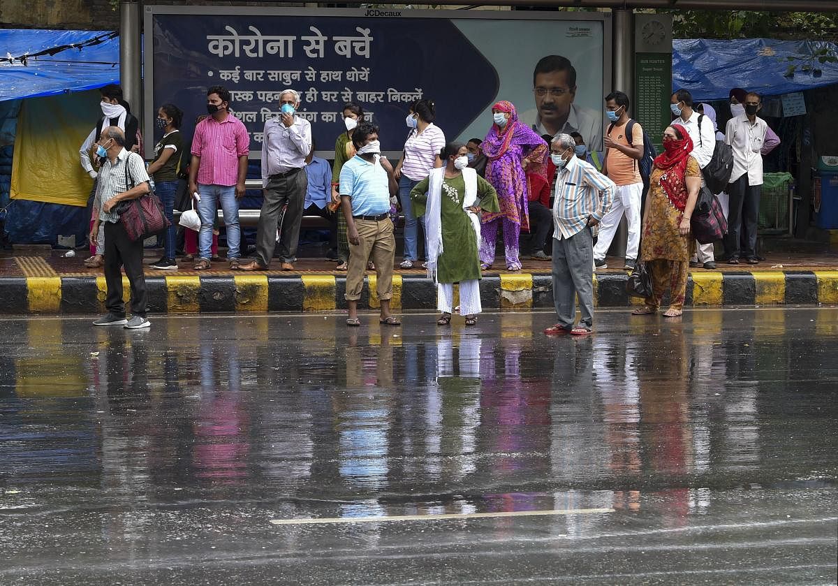 People wait for buses at a stop during monsoon rains, in New Delhi (PTI Photo)