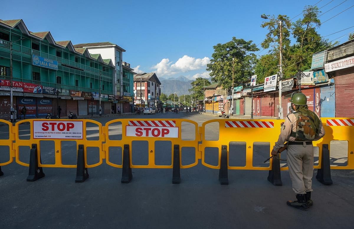 A security official stands guard on a blocked road after the authorities announced to re-impose lockdown from July 13 due to surge in Covid-19 cases, at Lal Chowk in Srinagar. Credit: PTI Photo