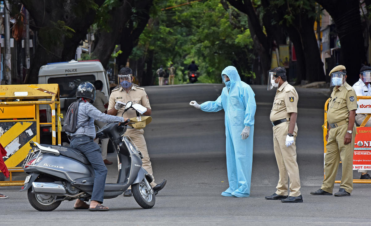 A policeman in a PPE kit asks a motorist to return home in view of the Sunday lockdown in Bengaluru. DH Photo/MS Manjunath