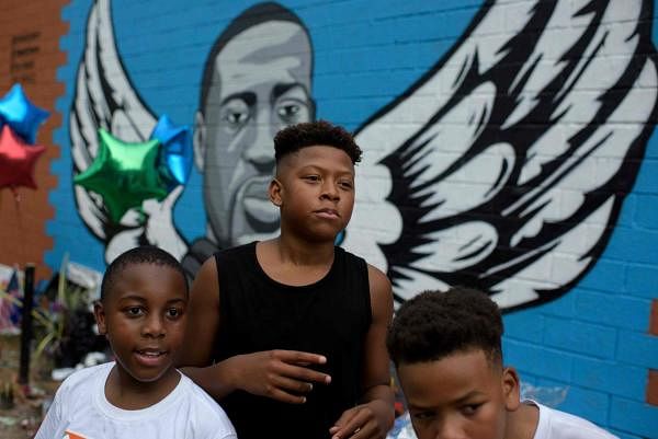 A groups of boys poses next to a mural of George Floyd. Credit: AFP