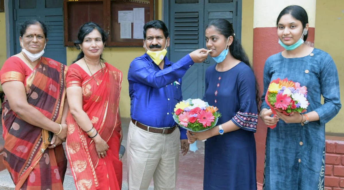 Principal B R Neelakanta greets Second PU toppers Spandana and Lakshmi of Marimallappa’s PU College in Mysuru on Tuesday. DH PHOTO