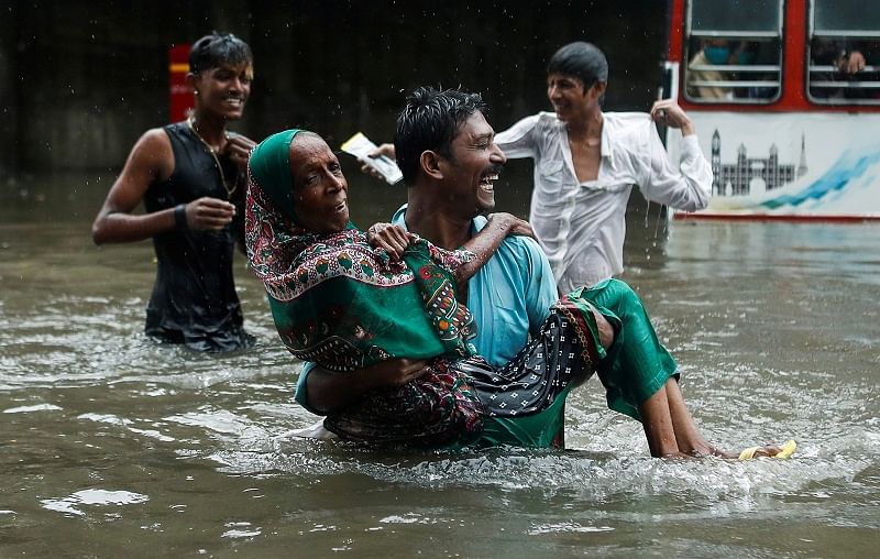 A man carries an elderly woman as they cross a waterlogged street during heavy rainfall in Mumbai, India. Credits: PTI Photo