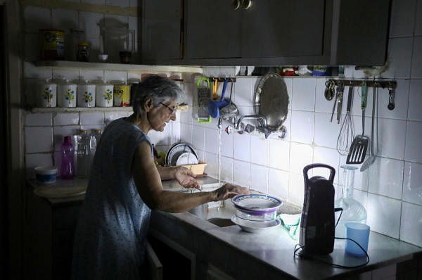 Samira Hanna, 70, washes dishes in her kitchen as she uses a portable electric light due to a power cut, in Beirut. Credit: Reuters