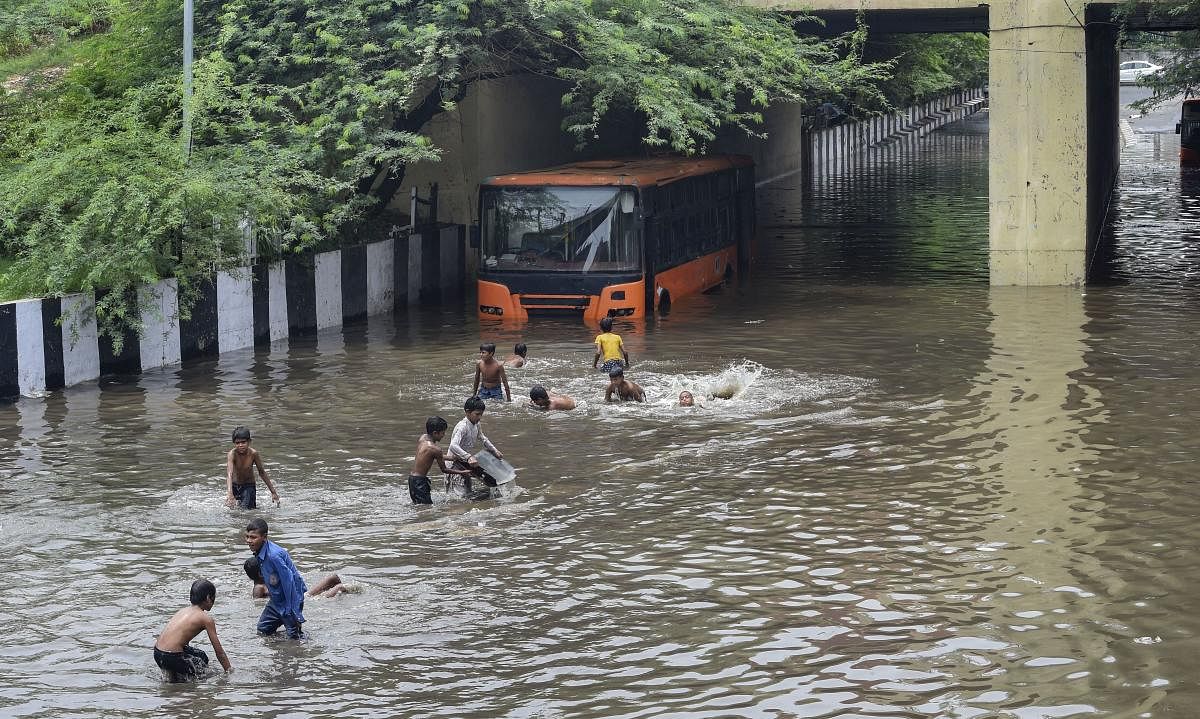A DTC bus stuck at waterlogged Zakhira underpass as children play, after rains in New Delhi. Credit: PTI FIle Photo