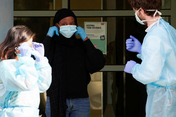 Healthcare workers assist a resident in putting her mask on outside of a public housing tower. Credit: Reuters Photo