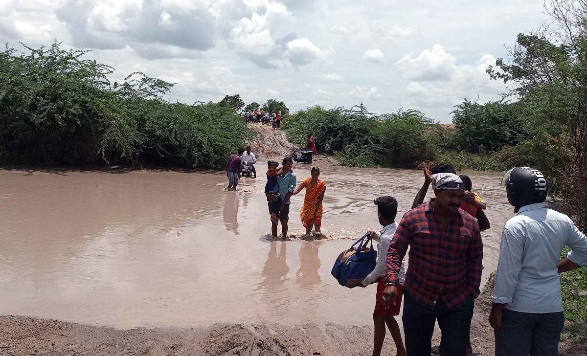 The residents of Bandral village in Siruguppa taluk, Ballari district, having a tough time in crossing a submerged low-lying bridge across a swollen stream, on Sunday. (Right) Water cascades down a hillock into Agastya Teertha pond in Badami following inc