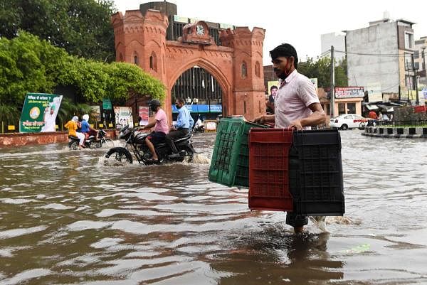 A man carrying crates wades along a water-logged street following heavy rains in Amritsar on July 19, 2020. Credit: AFP Photo