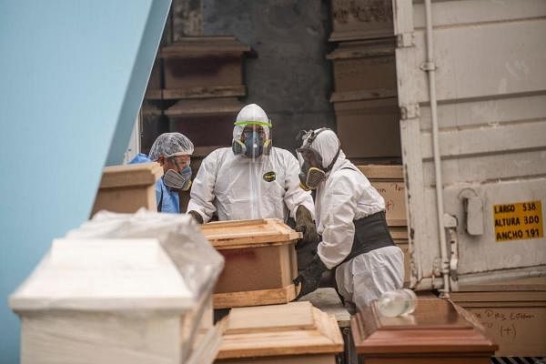 Workers move a coffin with the body of a Covid-19 victim out of a refrigerated container before its cremation. Credit: AFP