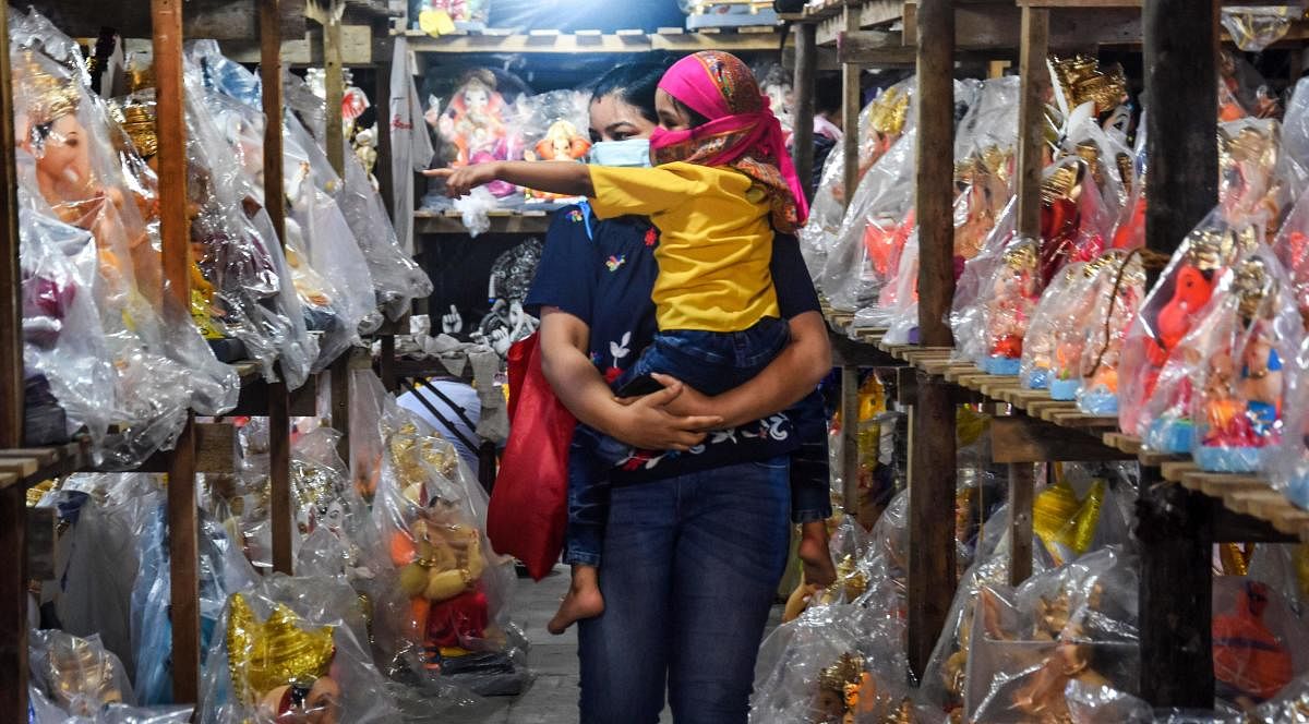 A woman carrying her child looks to purchase Lord Ganesha idol at a Ganpati workshop, during Unlock 2.0, at Andheri in Mumbai, Saturday, July 18, 2020. Credit: PTI Photo