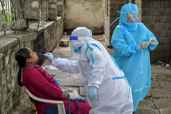 A health official (C) takes a swab sample from a patient at a Covid-19 point set up by Bangalore municipality. Credit: AFP Photo