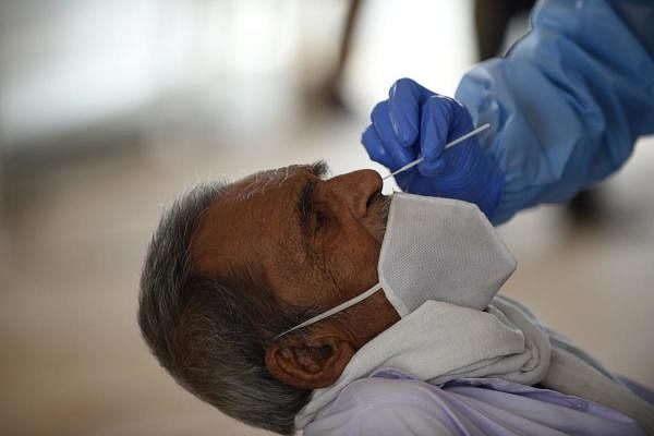 A health worker wearing a Personal Protective Equipment (PPE) suit takes a swab sample from a bus passenger for a COVID-19 coronavirus test at a makeshift test point at Sanathal, on the outskirts of Ahmedabad on July 17, 2020. Credit: AFP Photo
