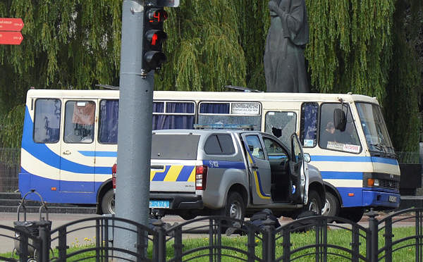 Ukrainian law enforcement officers lie on the ground behind a car near a passenger bus, which was seized by an unidentified person in the city of Lutsk, Ukraine. Credit: Reuters Photo