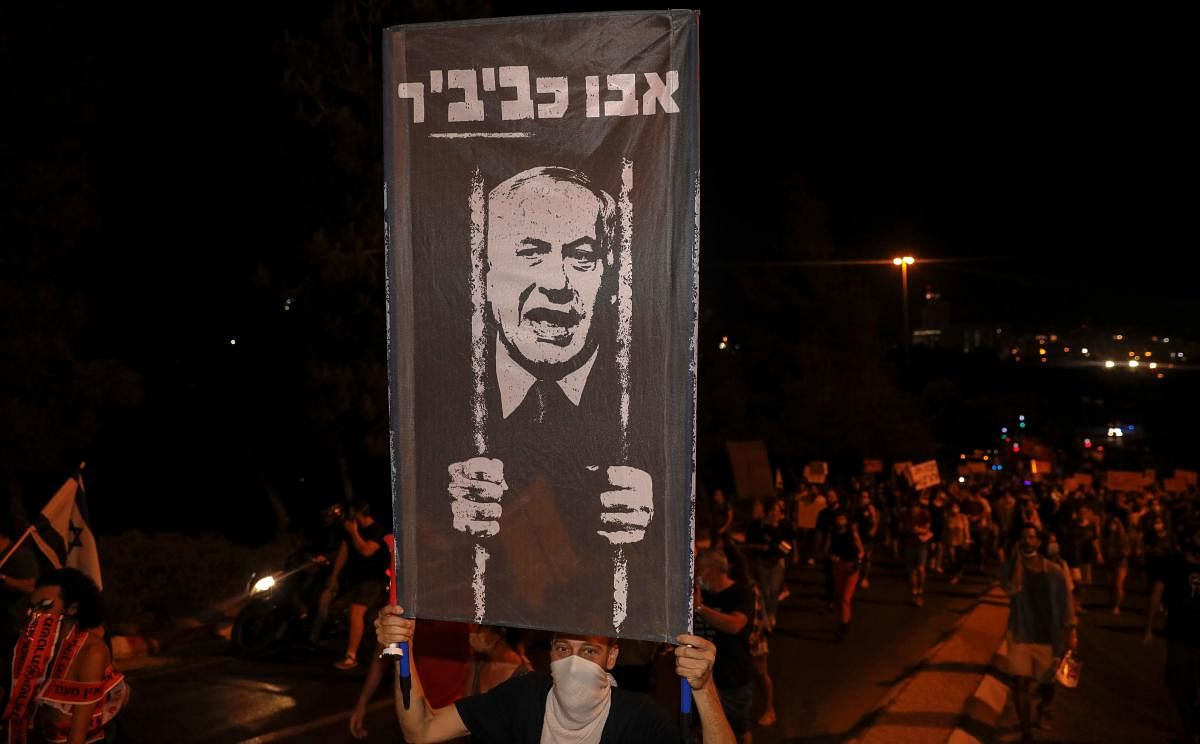 A protester wearing a face covering holds up a sign during a demonstration against the Israeli prime minister outside his official residence in Jerusalem. Credit: AFP photo