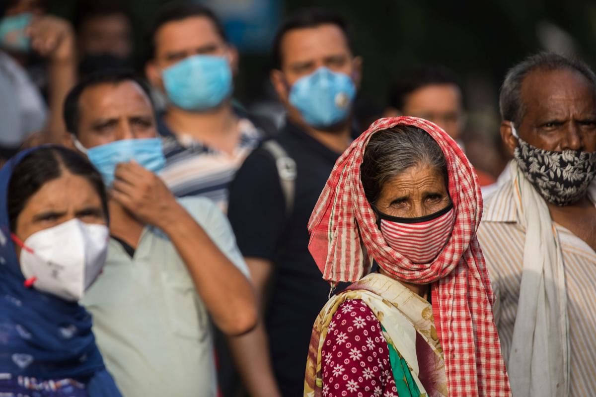 Commuters wearing face masks wait for bus after work during a rush hour in New Delhi on July 21, 2020. AFP