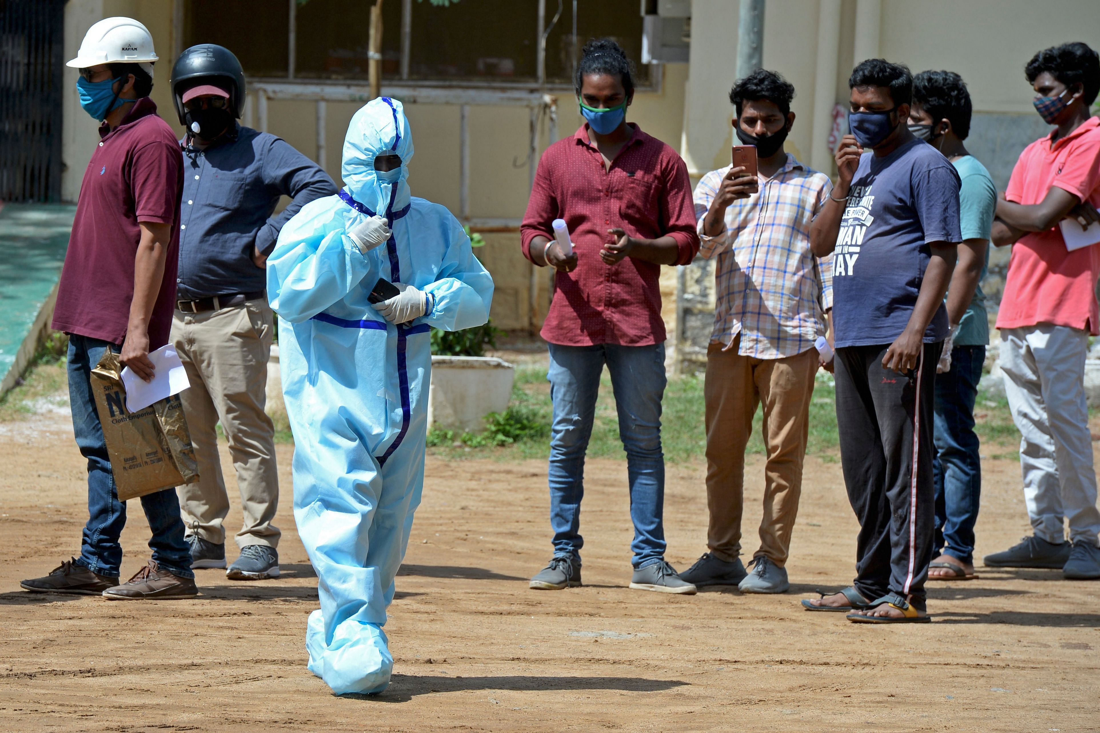 A health worker wearing Personal Protective Equipment (PPE) gear walks past the residents standing in queue to register their names at a free testing centre. Credit: AFP Photo