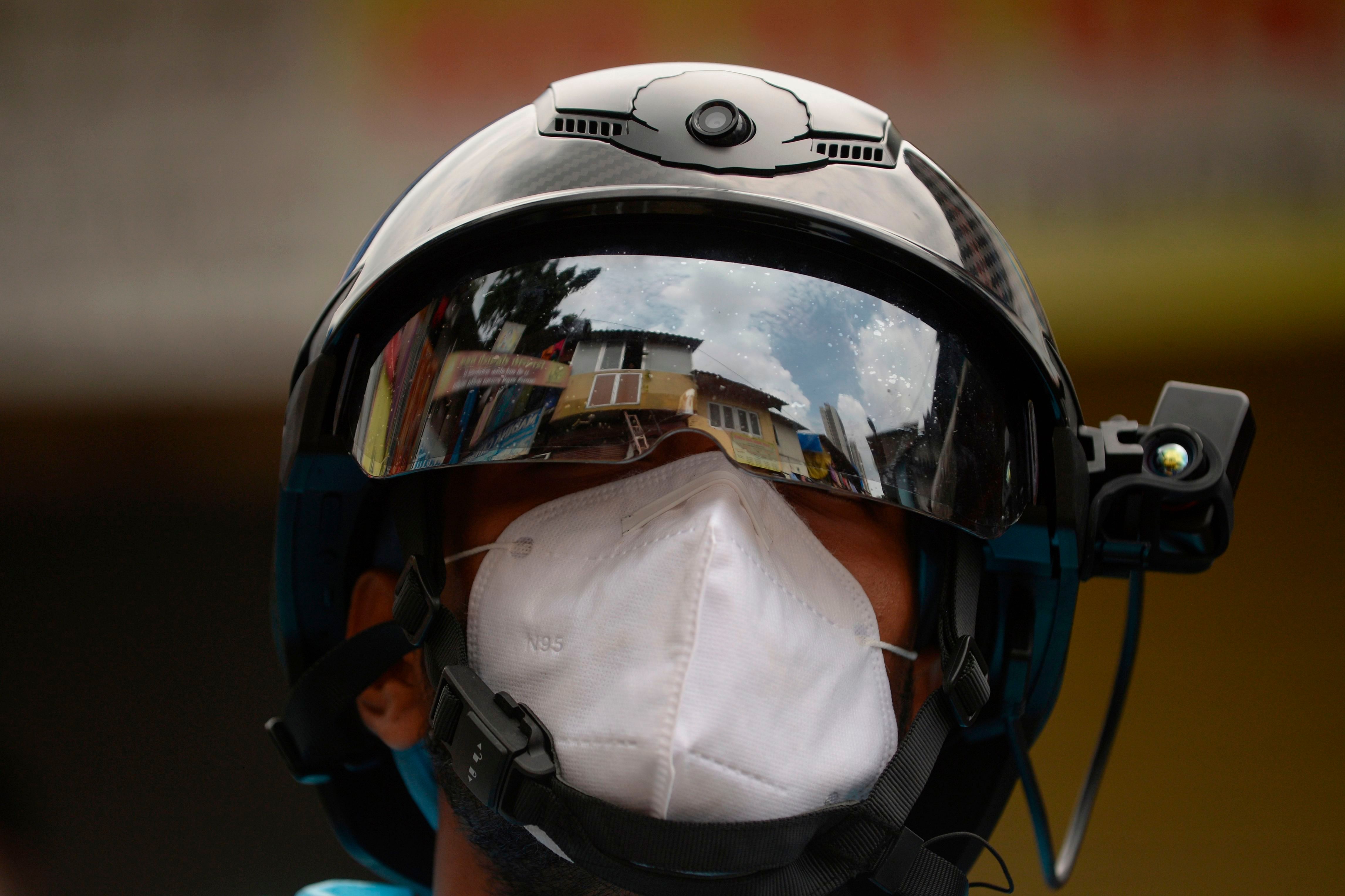 A volunteer health worker of the Non-Governmental Organization (NGO) Bharatiya Jain Sanghatana (BJS) wearing Personal Protective Equipment (PPE) looks through a smart helmet equipped with a thermo-scan sensor to check the body temperature during a door-to-door medical screening drive for the COVID-19 coronavirus, at a residential area in Mumbai. Credit: AFP