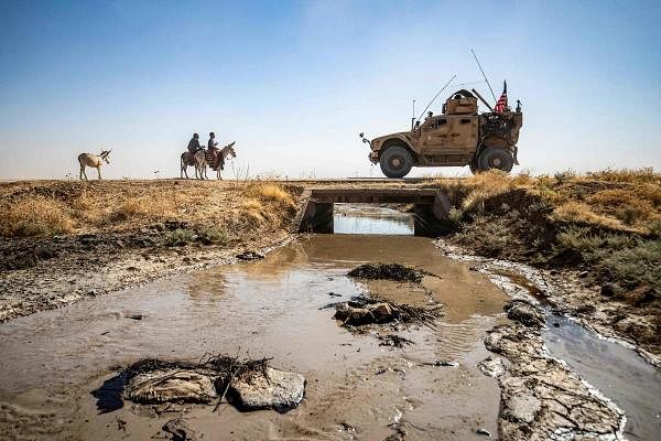 Youths ride donkeys near a US military vehicle crossing a stream polluted by an oil spill near the village of Sukayriyah, in the countryside south of Rmeilan. Credit: AFP