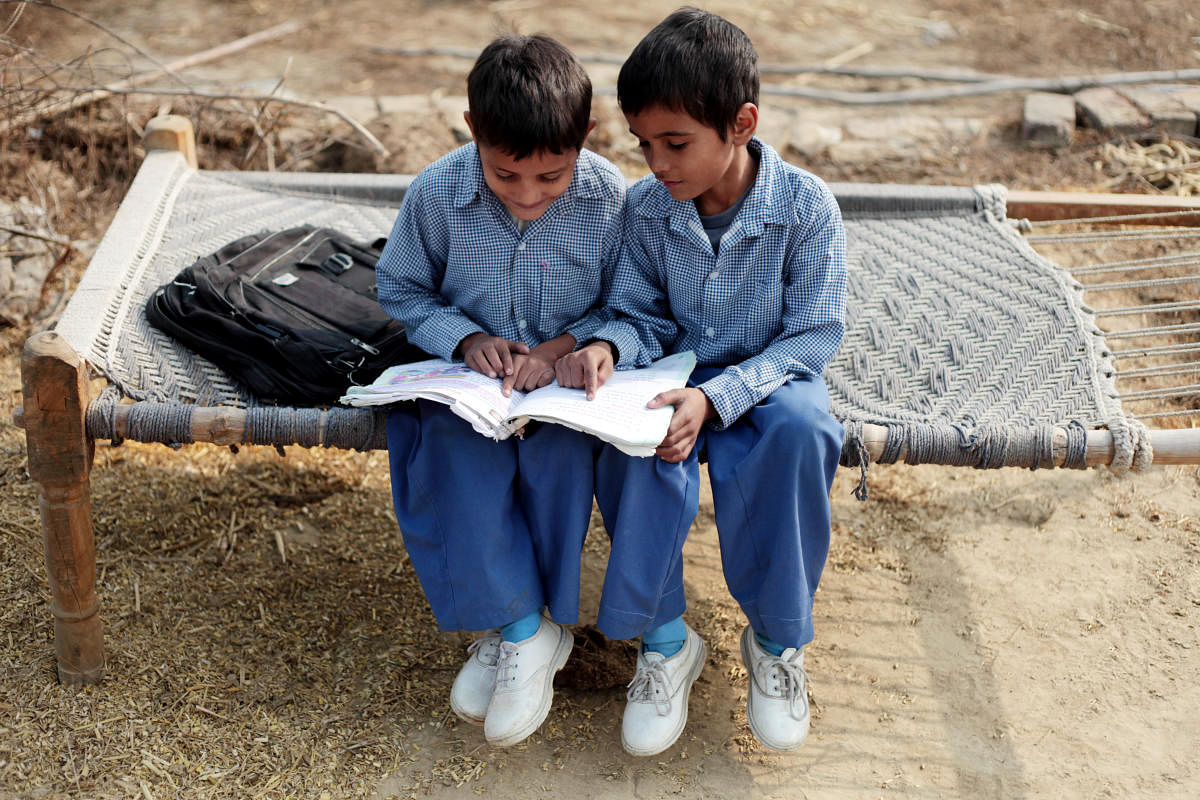 Two rural children sitting on a cot and reading a book carefully.