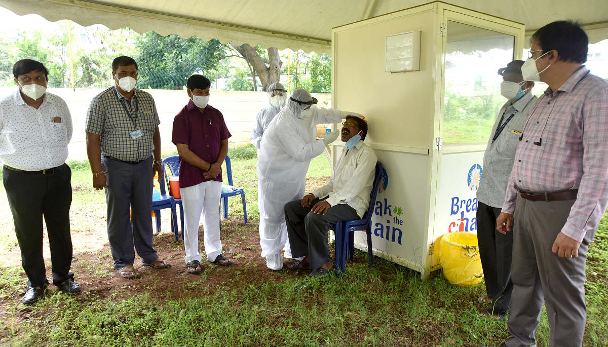 Health department officials collect throat swab of a person for Covid-19 test at the swab collection centre at Makkala Koota in Krishnamurthypuram, Mysuru, on Thursday. MLA S A Ramadas is seen.