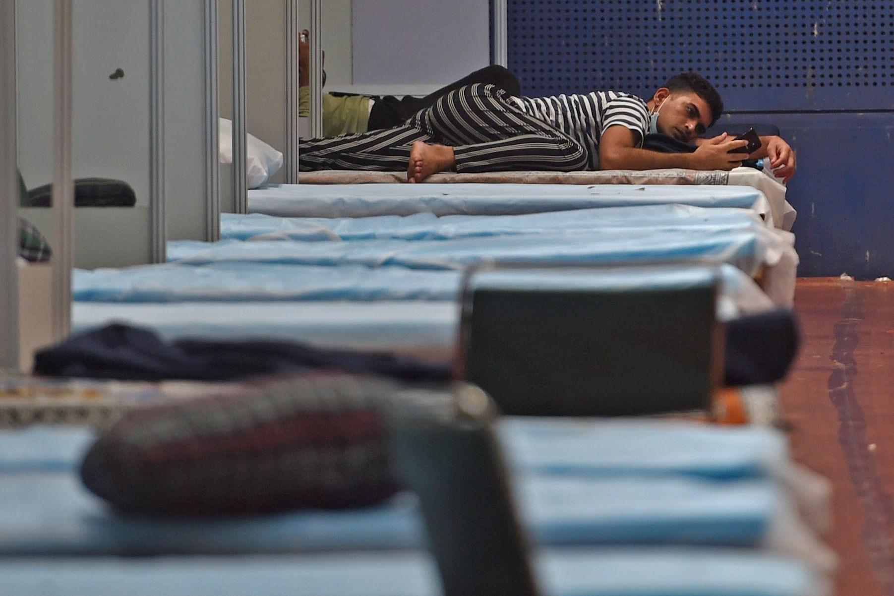 A patient looks at his mobile phone inside a ward at the Commonwealth Games (CWG) Village sports complex, temporarily converted into COVID-19 care. Credits: AFP Photo