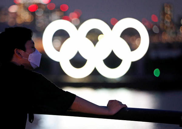 The giant Olympic rings are seen through visitors wearing protective face masks amid the coronavirus disease. Credit: Reuters