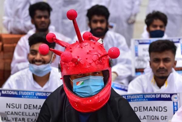 A member of NSUI wears coronavirus theme-based helmet during a protest, demanding the cancellation of final year exams of UG, PG and VTU and to postpone the Karnataka CET, in front of Raj Bhawan in Bengaluru, Friday, July 24, 2020.  Credit: PTI Photo