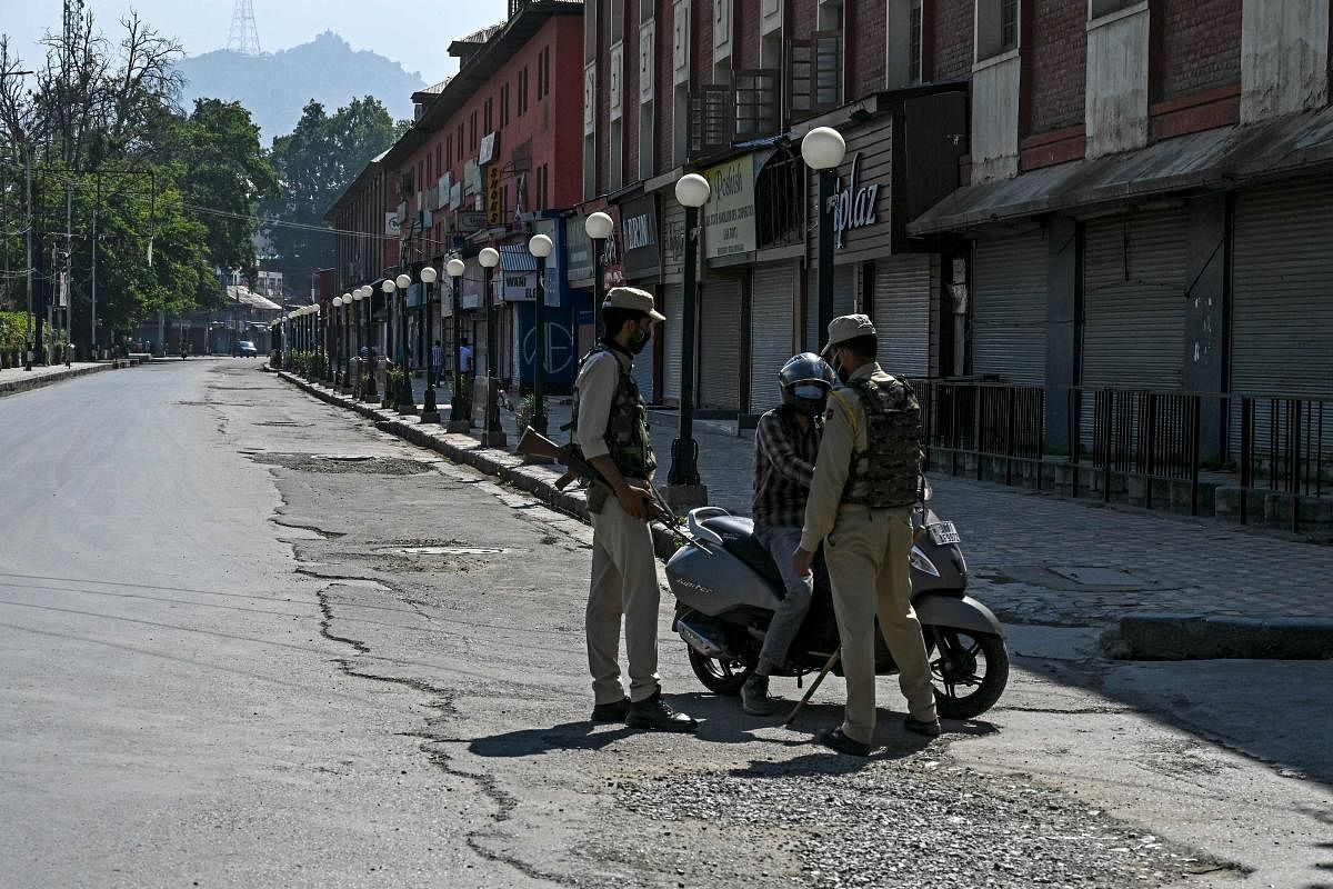 Security personnel stop a motorcyclist (C) on an empty street of a closed market during a lockdown imposed by the authorities as a preventive measure against the surge in coronavirus cases, in Srinagar on July 23, 2020. Credit: AFP Photo