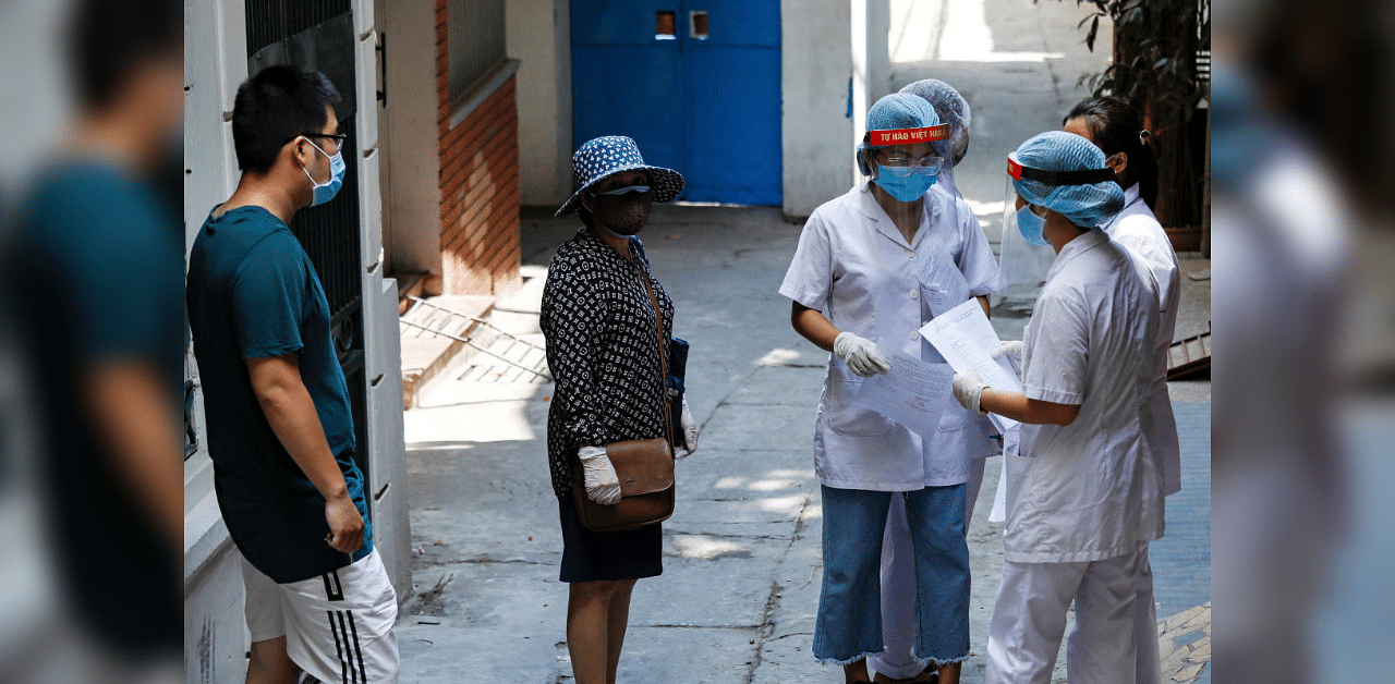 Healthcare workers talk to a local resident near the house of a coronavirus disease patient as they investigate infection links in Vietnam. Credit: Reuters