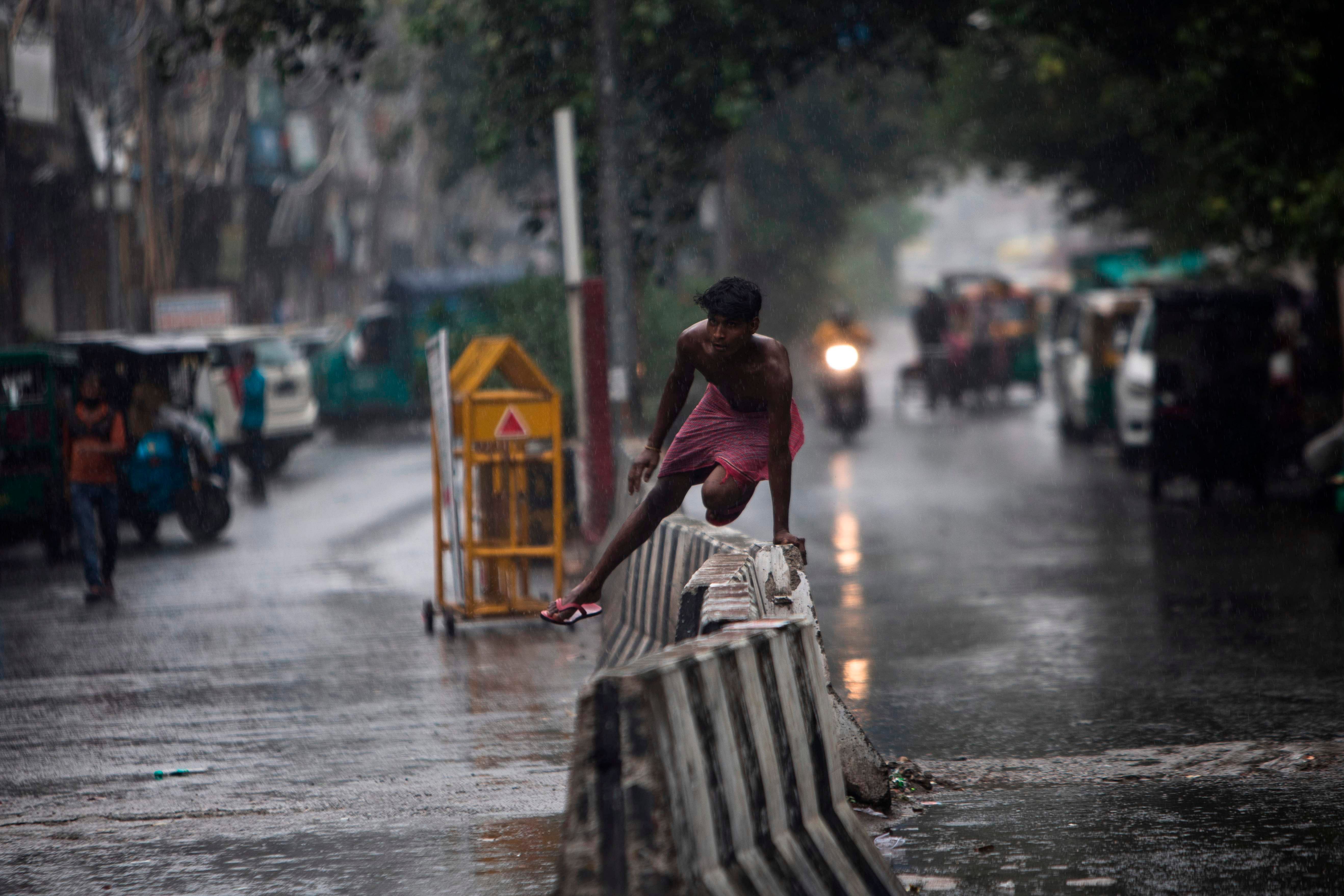 A youth jumps over a concrete barrier along a street during a monsoon rainfall in New Delhi. Credits: AFP Photo
