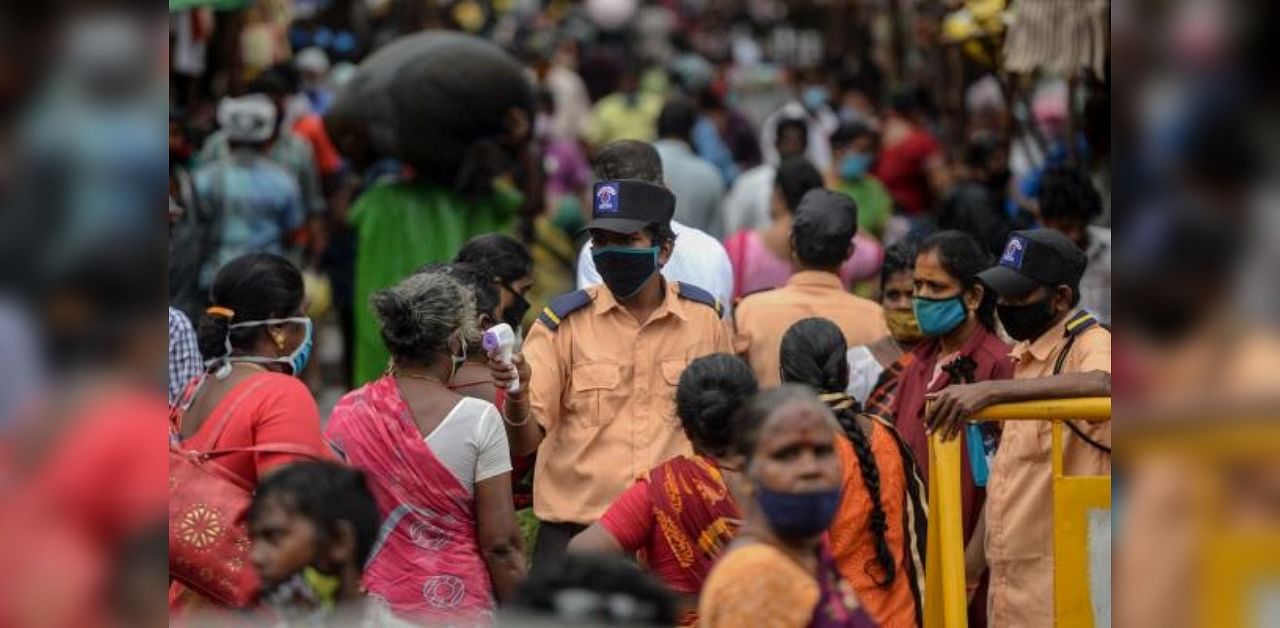 A security personnel (C) checks the body temperature of a woman (C-L) as she enters a market among a crowd of people as a preventive measure against the spread of the COVID-19 coronavirus in Chennai on July 29, 2020. Credit: AFP Photo