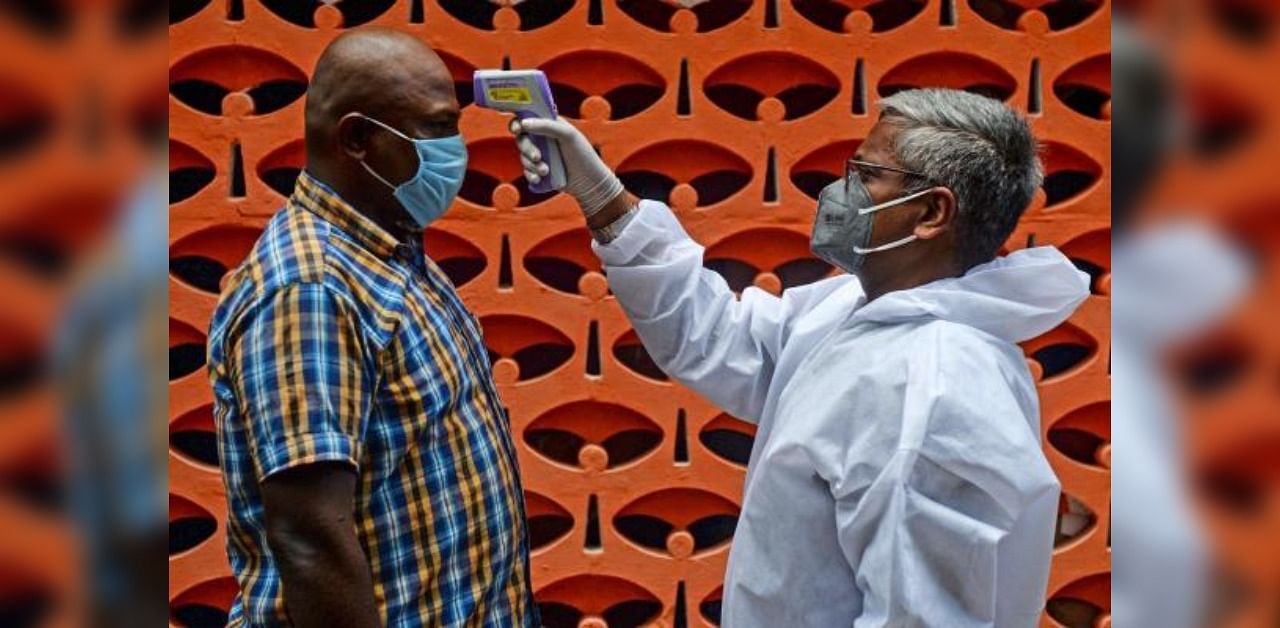 A doctor (R) checks the body temperature of a man at a containment zone implemented as a preventive measure against the Covid-19 coronavirus in Chennai. Credit: AFP Photo