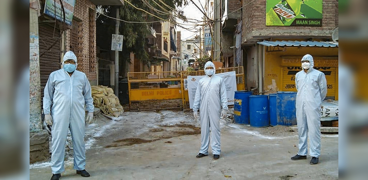 Police personnel wearing protective suits stand guard at a Covid-19 containment zone in South Delhi. Credit: PTI File Photo