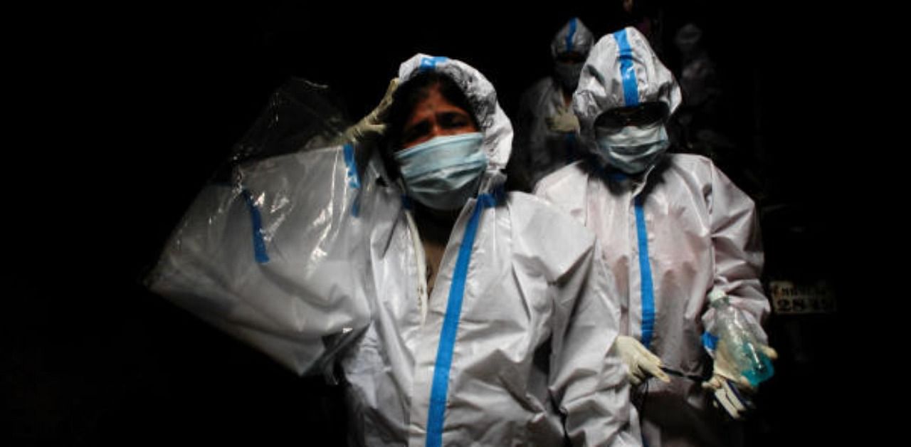 A health worker in personal protective equipment reacts as she and the rest of the team walk through an alley during a check up campaign for the coronavirus disease. Credit: Reuters