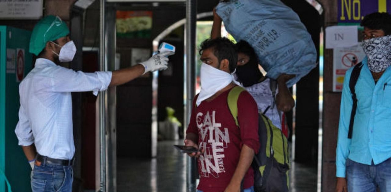 A worker wearing a protective face mask checks the temperature of a traveller. Credit: Reuters