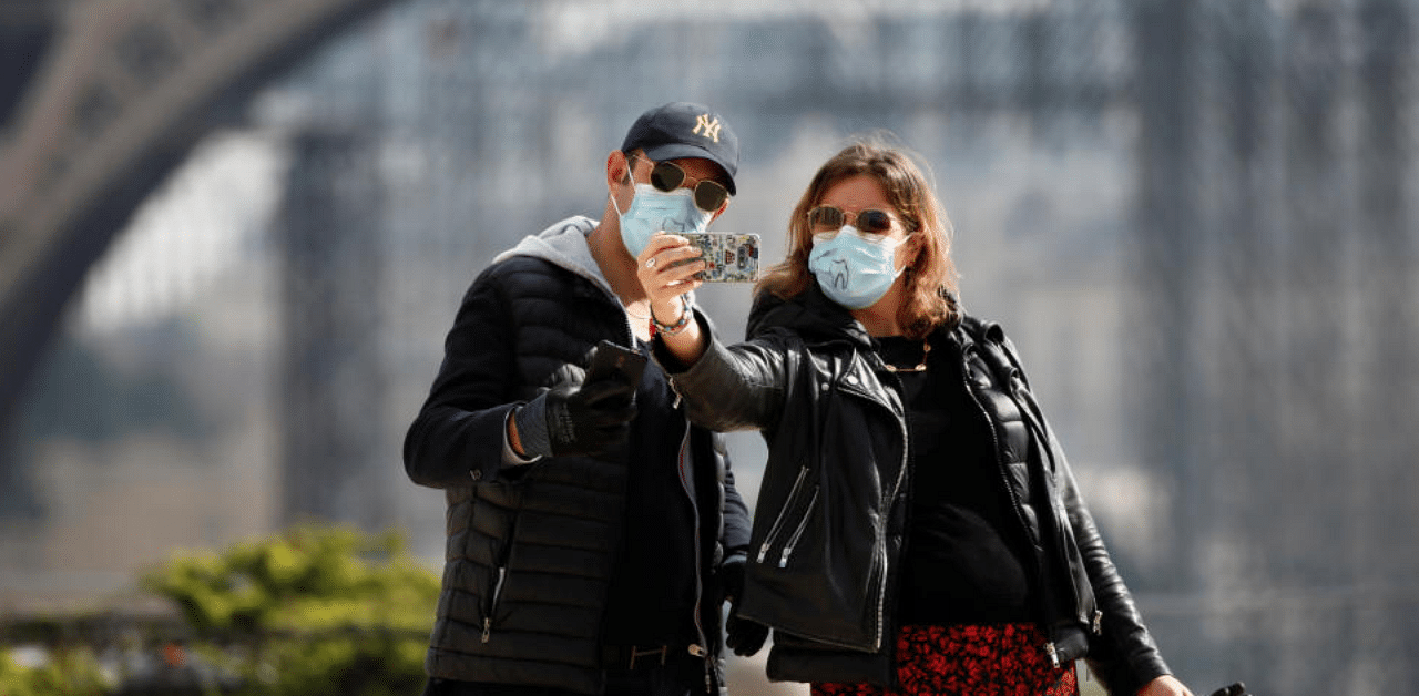 A couple wearing protective masks take a selfie in front of the Eiffel Tower as lockdown is imposed to slow the spreading of the coronavirus disease in France. Credit: Reuters Photo