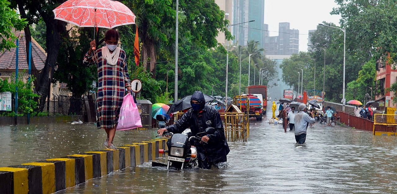 A motorist pushes his stalled bike while a lady walks on a road divider during a heavy monsoon rainfall in Mumbai. Credit: AFP Photo