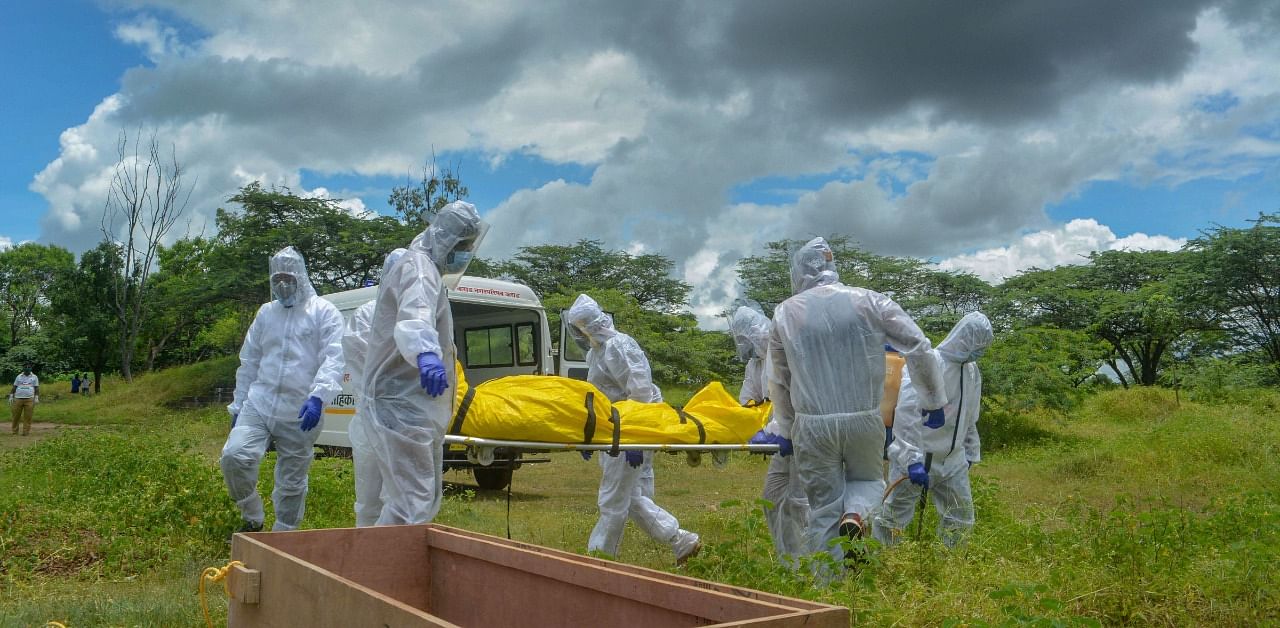 Municipality workers and family members wearing protective suits carry the body of a person who died of Covid-19 for the burial at a graveyard. Credit: PTI Photo