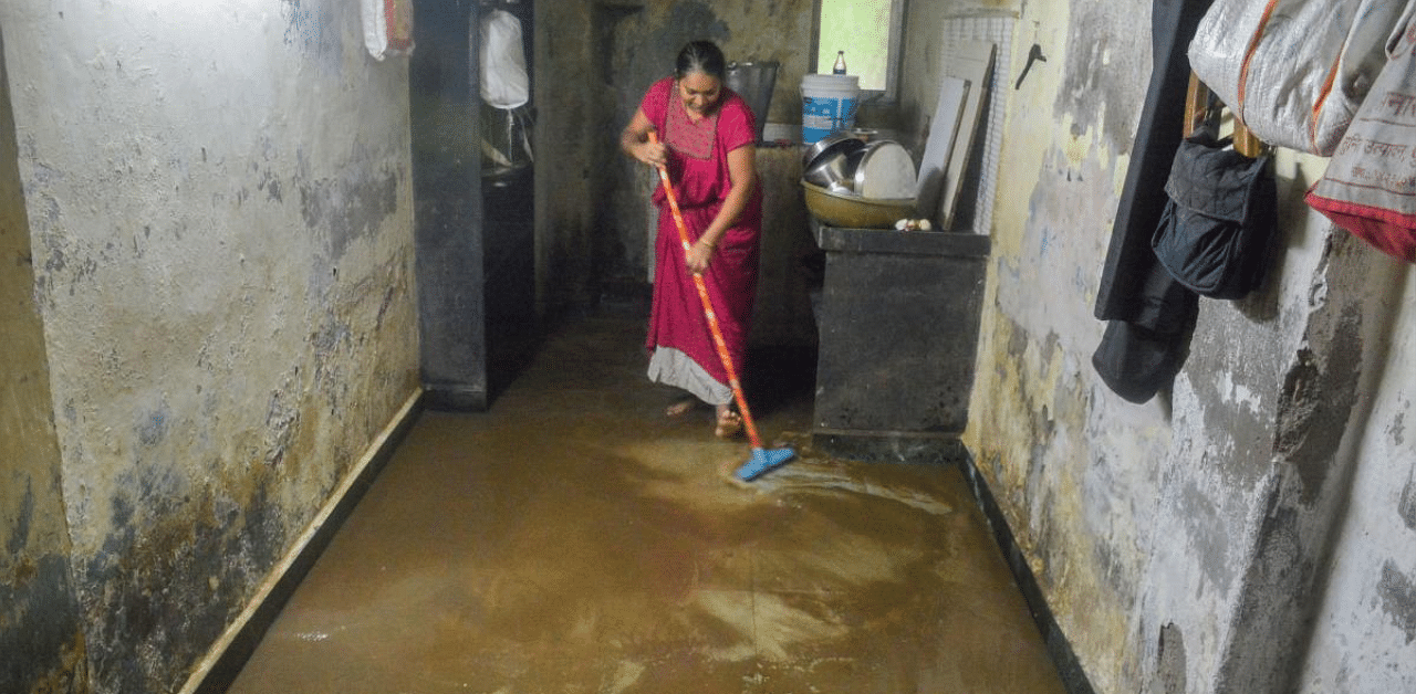 A woman tries to remove rain water from her flooded house after heavy rains in Thane. Credit: PTI