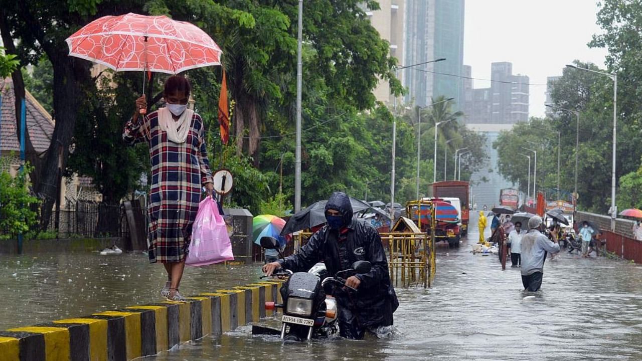 A motorist pushes his stalled bike while a woman walks on a road divider during a heavy monsoon rainfall in Mumbai. Credit: AFP