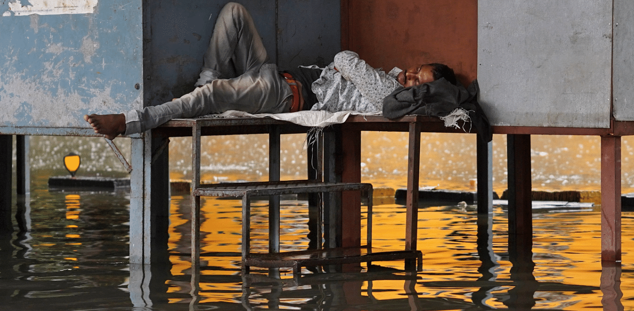 A man sleeps outside a temporary municipal office on a flooded street during heavy rains in Mumbai. Credits: Reuters Photo