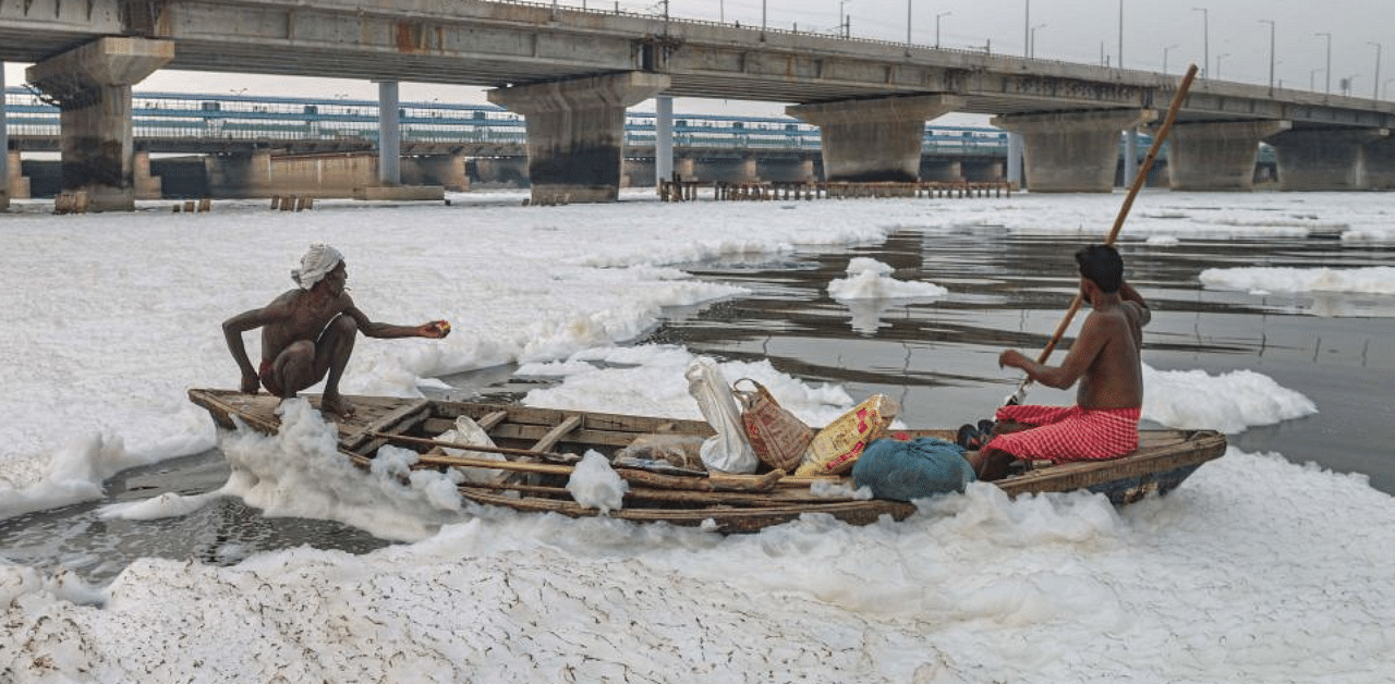 Fishermen row their boat across the froth covered Yamuna river. Credit:PTI