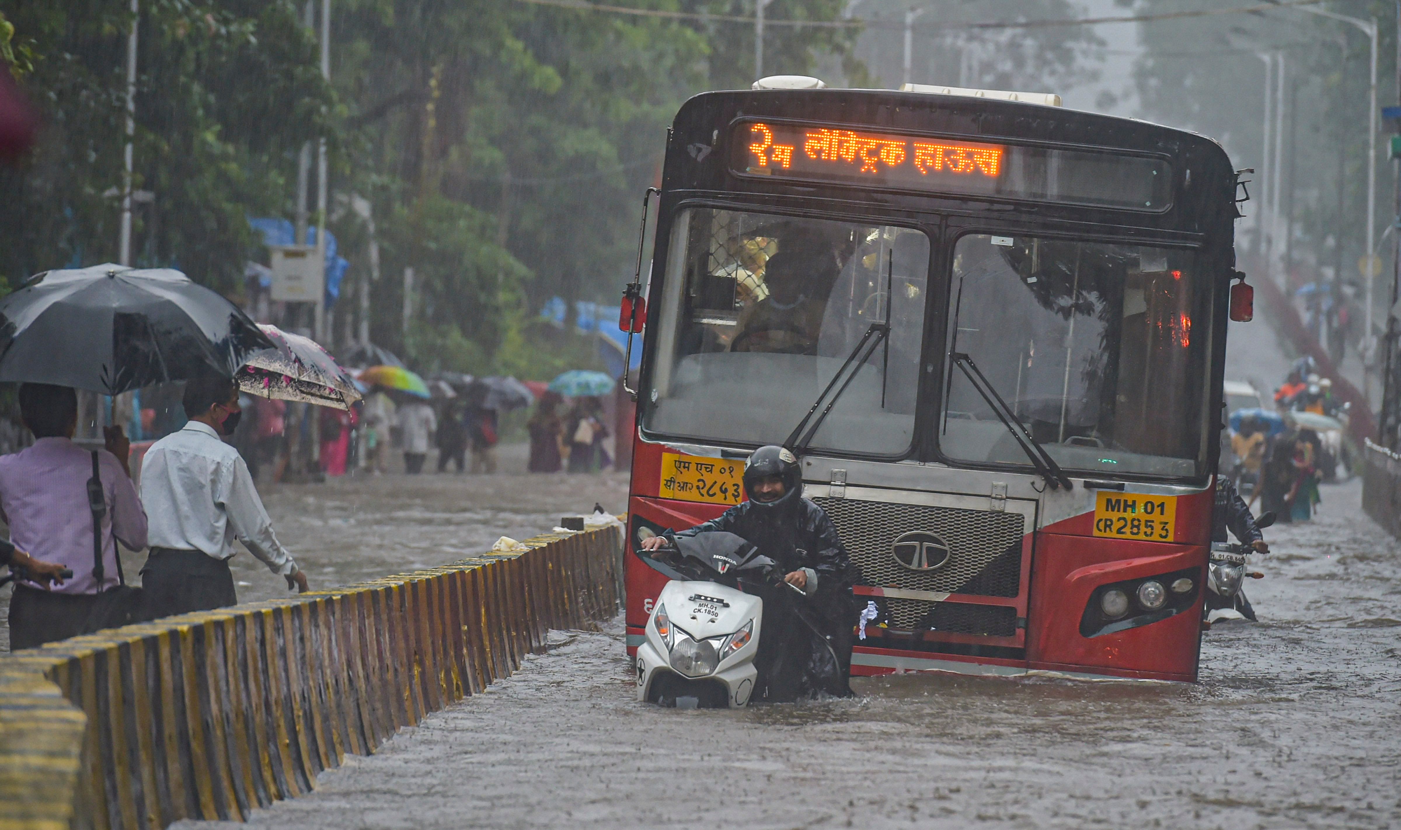Commuters make way through a waterlogged road during rain, in Mumbai. Credit: PTI