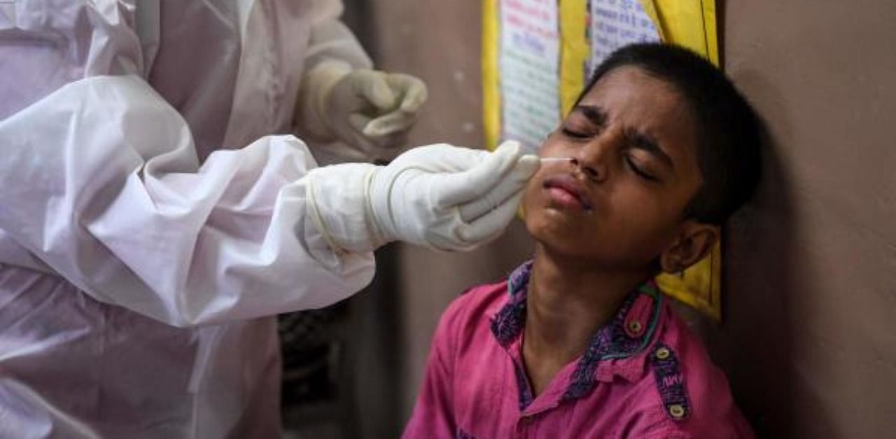 A medical staff (L) takes a sample from a young boy for a Rapid Antigen Test (RAT) for the coronavirus. Credit: AFP
