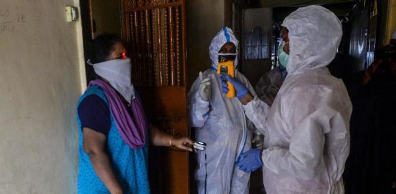 A health worker (R) wearing a Personal Protective Equipment (PPE) checks the body temperature of a resident (L) during a door-to-door coronavirus screening in a building in Dharavi slum area in Mumbai. Credit: AFP