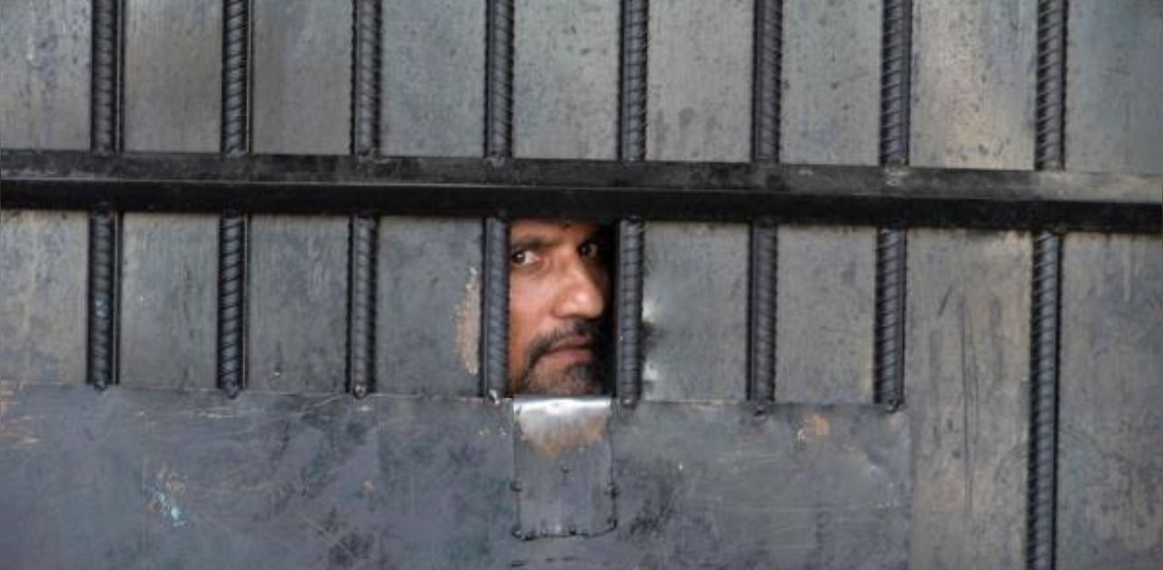 An inmate watches from behind a closed gate after a raid at the prison in Jalalabad. Credit: AFP