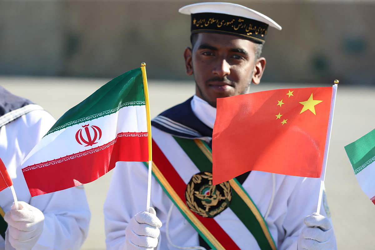 A handout photo made available by the Iranian Army office on December 27, 2019 shows an Iranian seaman holding up Iranian and Chinese national flags during a ceremony at Chabahar on the Gulf of Oman during Iran-Russia-China joint naval drills. - Iran, Chi